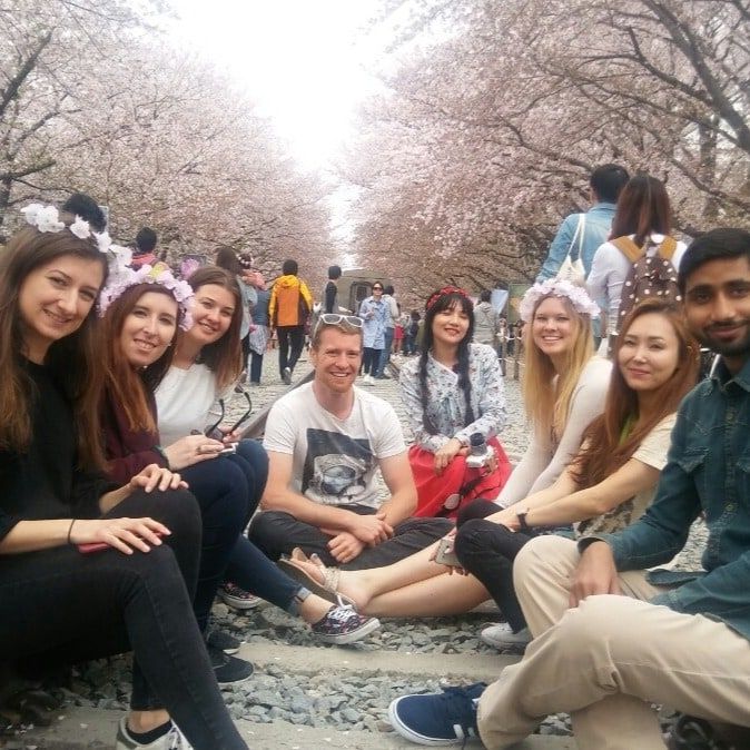 A group of travellers in flower crowns sitting on railway tracks under cherry blossom