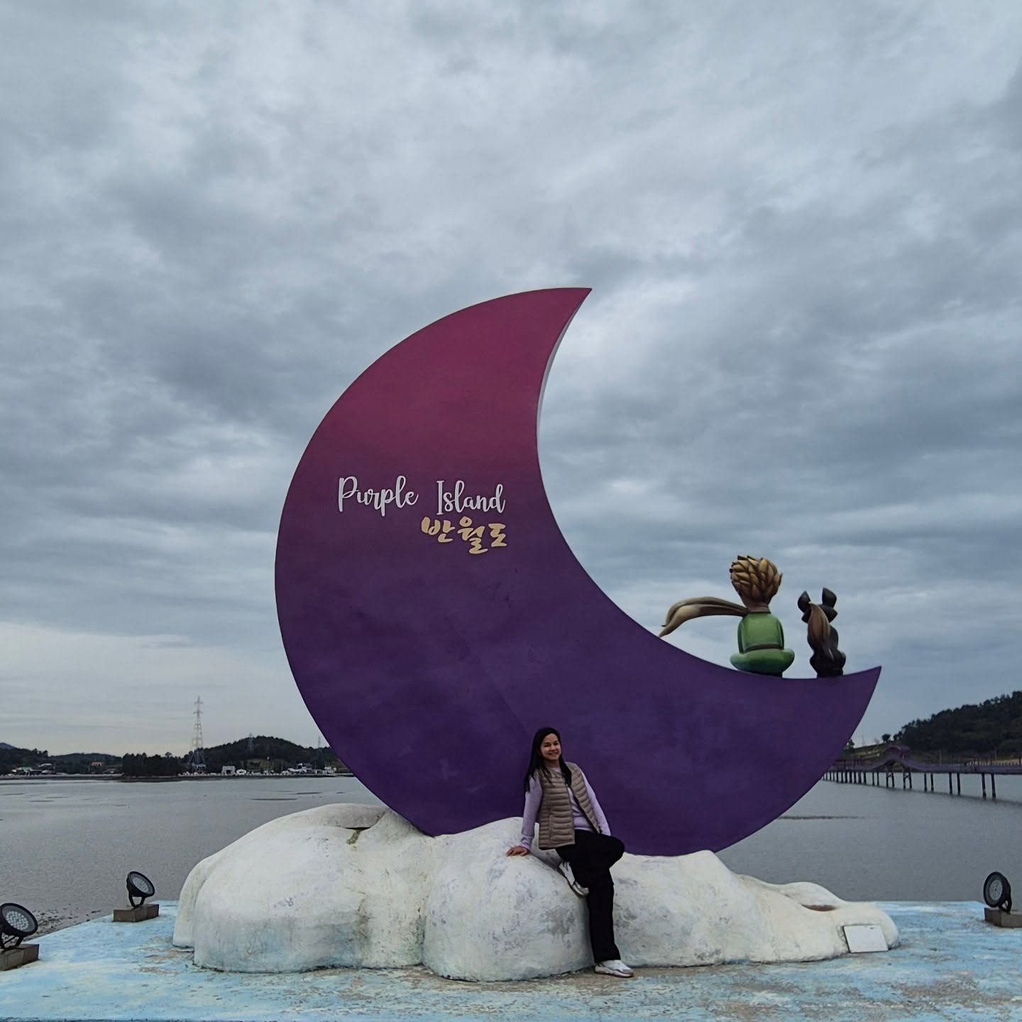 A traveller sitting under the giant purple moon sculpture signed “Purple Island 반월도”